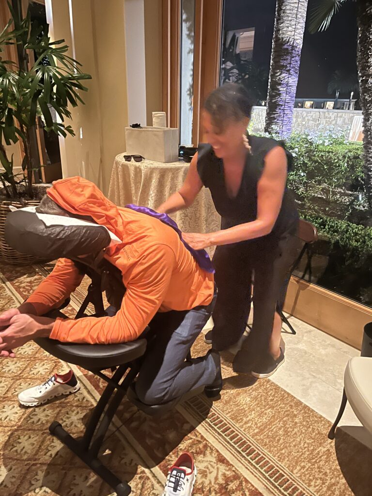 A man seated in a chair receives assistance from a woman, highlighting the benefits of chair massages for tension relief.