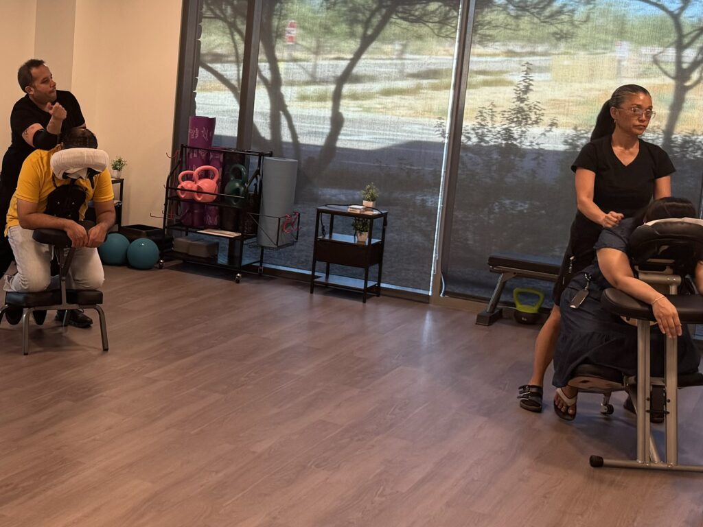 A group of individuals in an office room, with a chair, discussing the benefits of massage for stress relief.