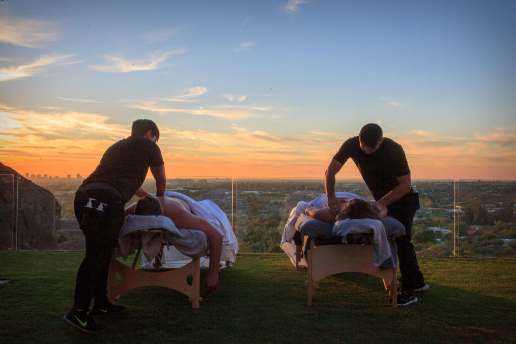 Two men receive soothing massages on a grassy field, symbolizing relaxation and connection for the New Year.