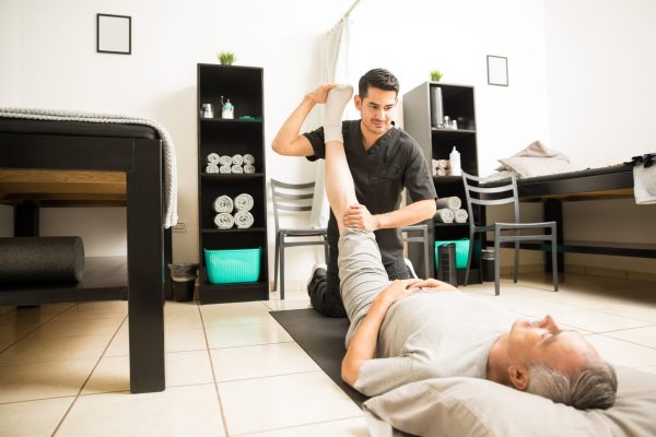 physiotherapy-doctor-assisting-elderly-patient-with-leg-exercise-clinic (1)